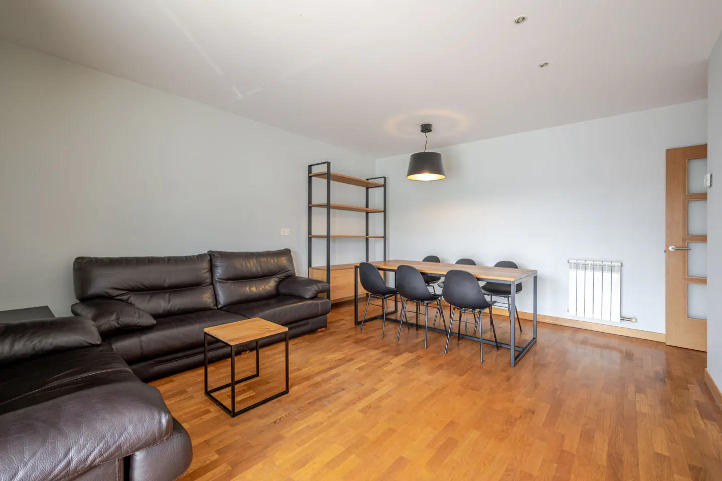 Living room with a brown leather sofa, wood table, black chairs, and wood floors.