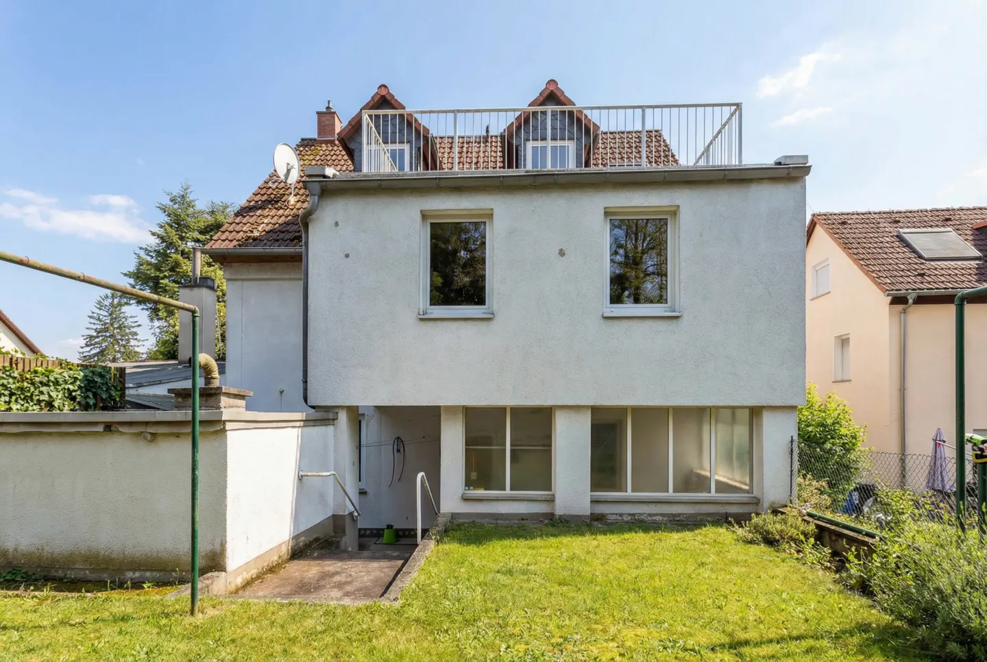 Back of a white two-story house with a rooftop deck, windows, and a green lawn.