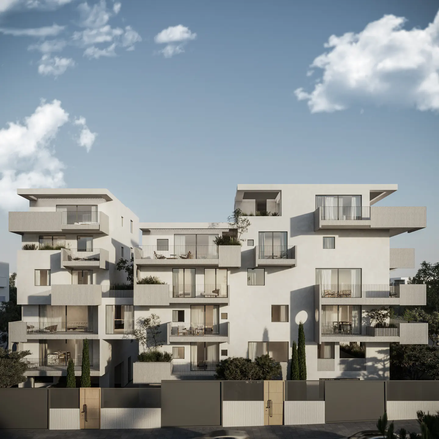 Modern white apartment building with balconies under a blue sky. Trees and a gray fence are in the foreground.