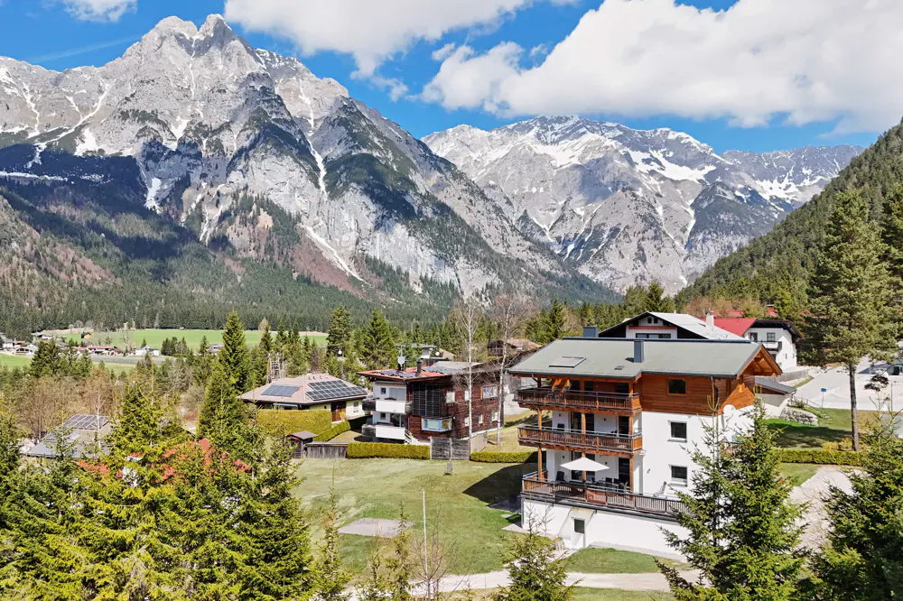 Scenic view of alpine houses nestled in a valley with snow-capped mountains in the background.