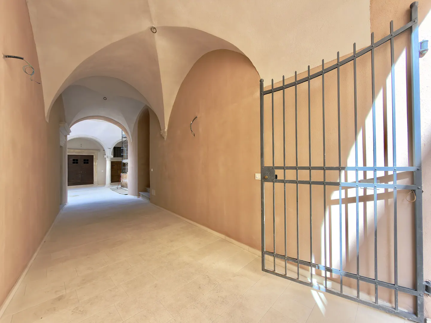 Arched hallway with beige walls and light tile floor. A metal gate is on the right, partially open.