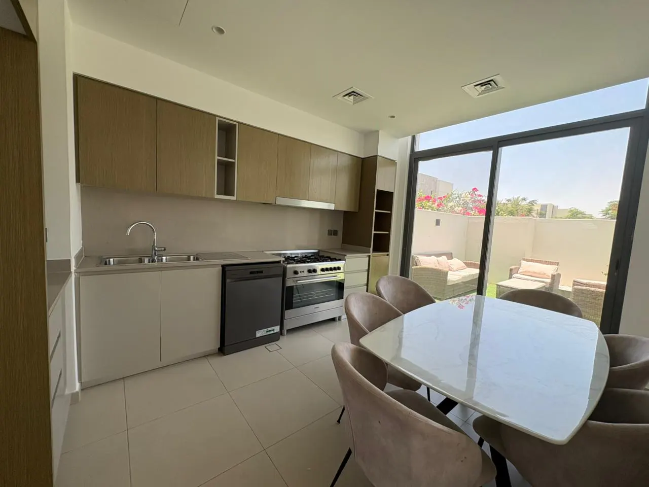 A bright kitchen with a white table and chairs, stainless steel appliances, and a view of an outdoor patio.
