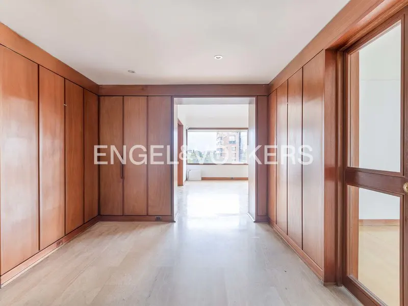 An empty room with wood paneling and marble floors. A doorway leads to a bright room with a large window.