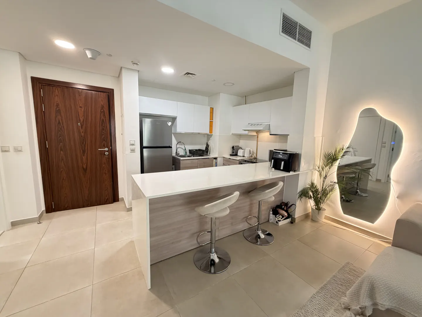A modern apartment interior with a kitchen island, white cabinets, and a unique illuminated mirror.