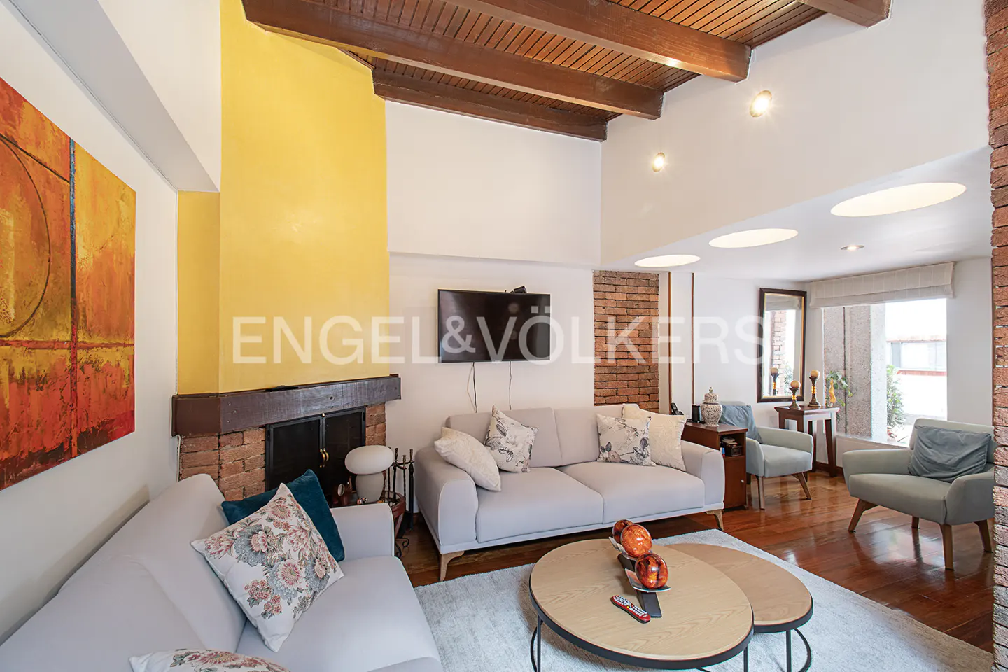 Living room with light gray sofas, round coffee tables, and a brick fireplace with a yellow accent wall.