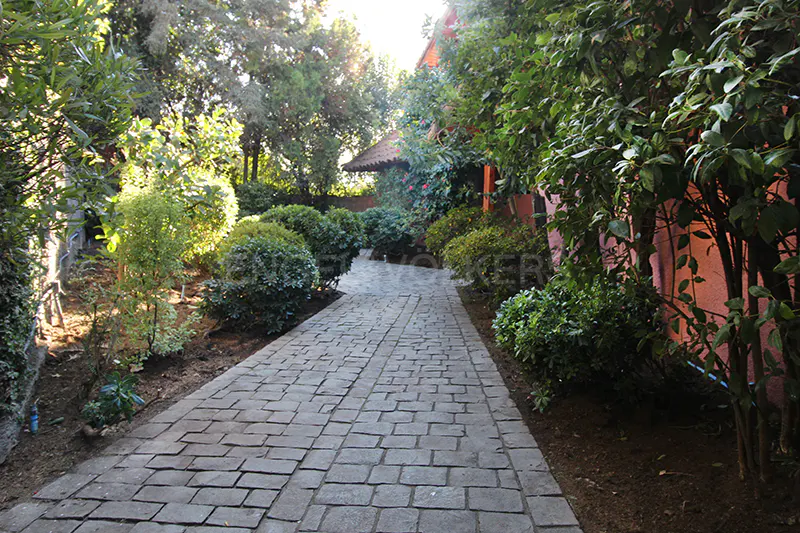 A stone path leads through lush green landscaping to a house with a red roof.