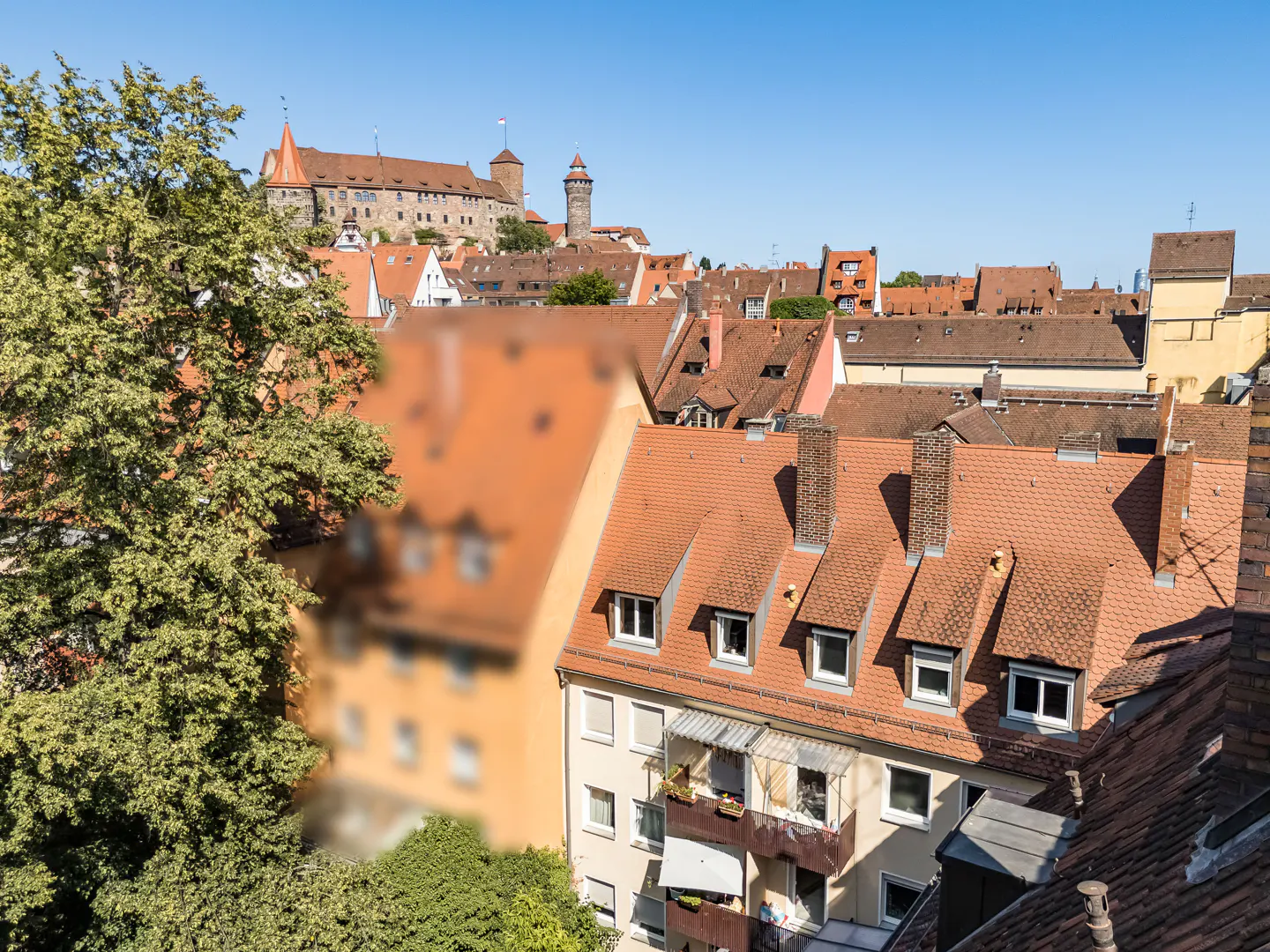 View of Nuremberg, Germany, with red-tiled roofs, a castle on a hill, and a clear blue sky.