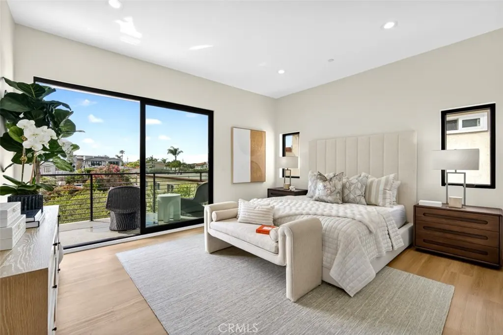 Bright bedroom with a king bed, bench, and balcony. Large sliding glass doors offer a view of the neighborhood.