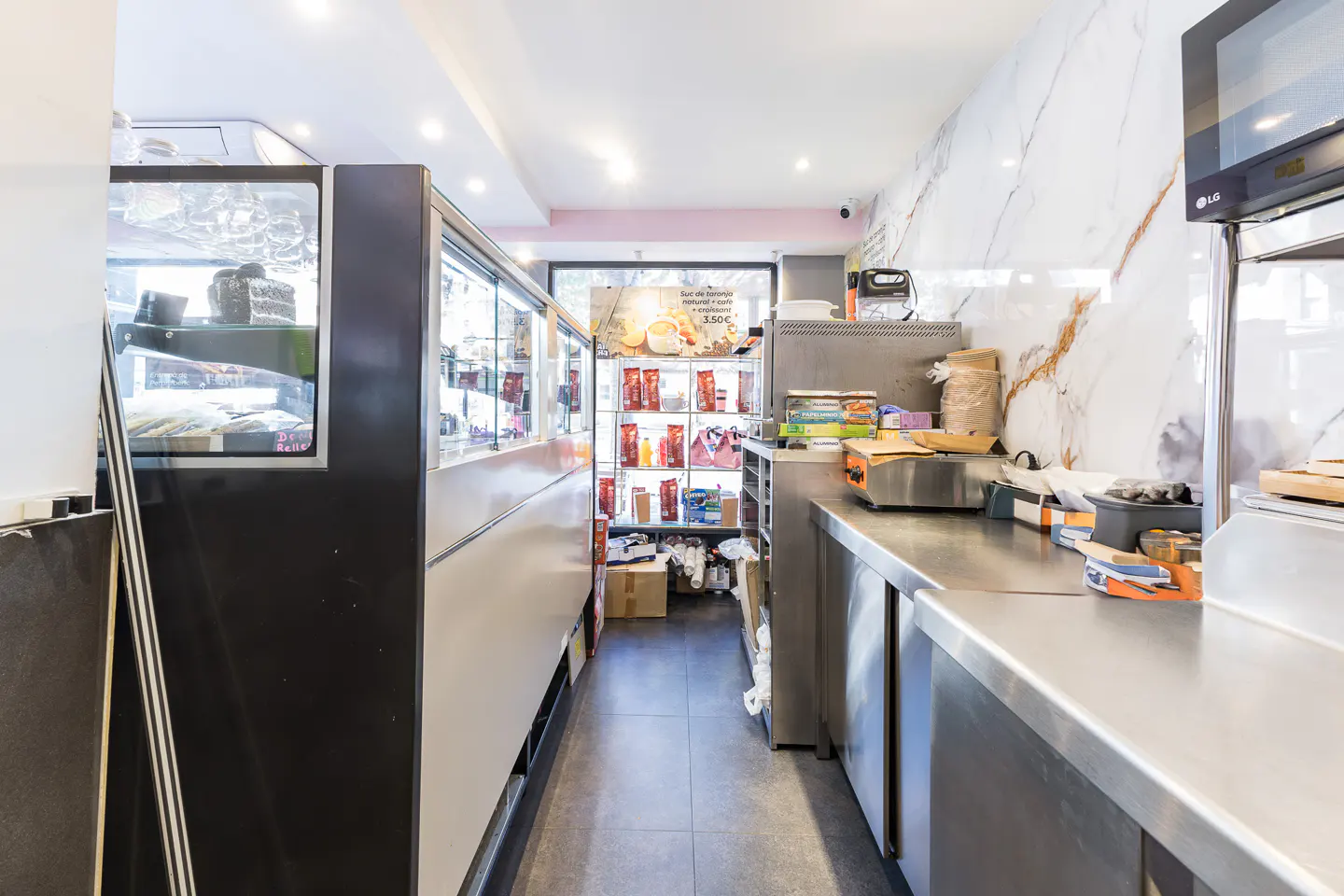 A bakery interior with a display case filled with cakes, a stainless steel counter, and shelves of packaged goods.