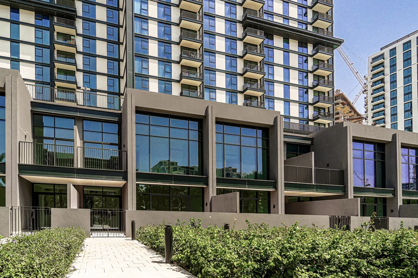 Exterior view of modern townhouses with large windows and balconies, set against a backdrop of a high-rise building.