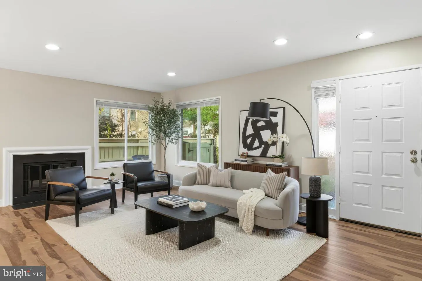 Living room with wood floors, a fireplace, two black chairs, and a light gray sofa on a white rug. A black coffee table sits in the center.
