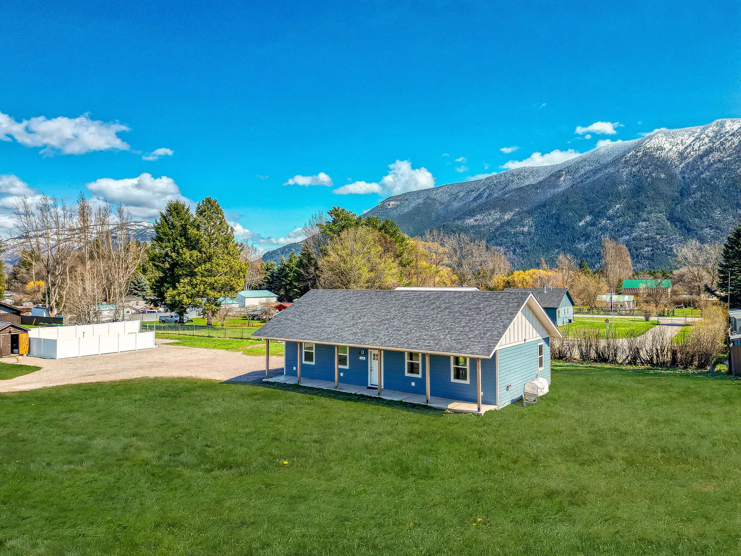 Blue house with a gray roof and white trim, surrounded by a green lawn, with mountains in the background.