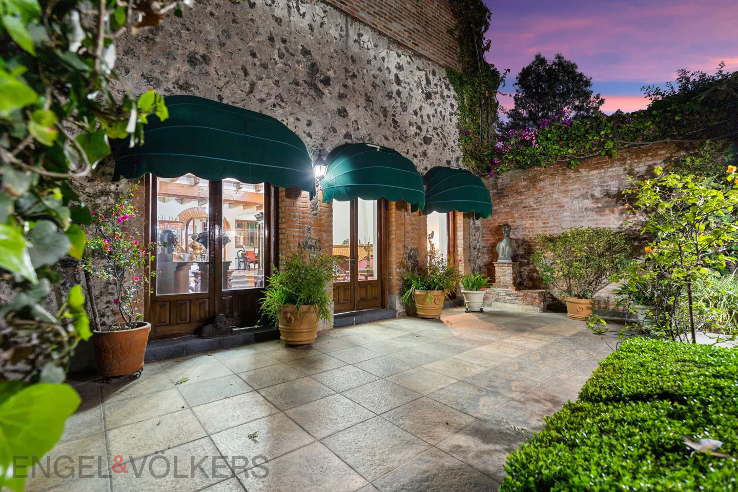 Exterior of a stone building with three arched doorways, each with a green awning, and potted plants.