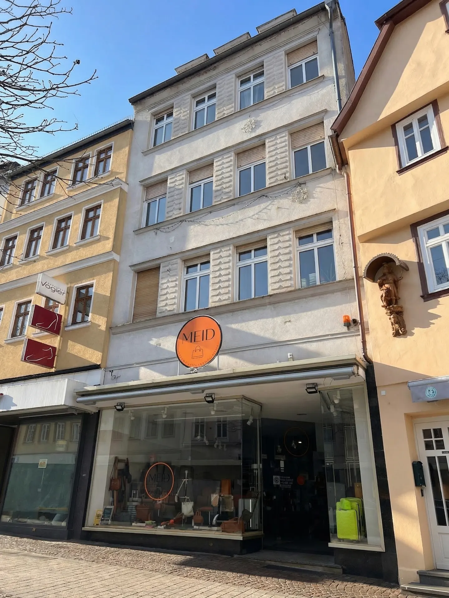 A three-story building with a storefront and an orange sign that reads "MEID" is shown. The building is flanked by yellow buildings on either side.