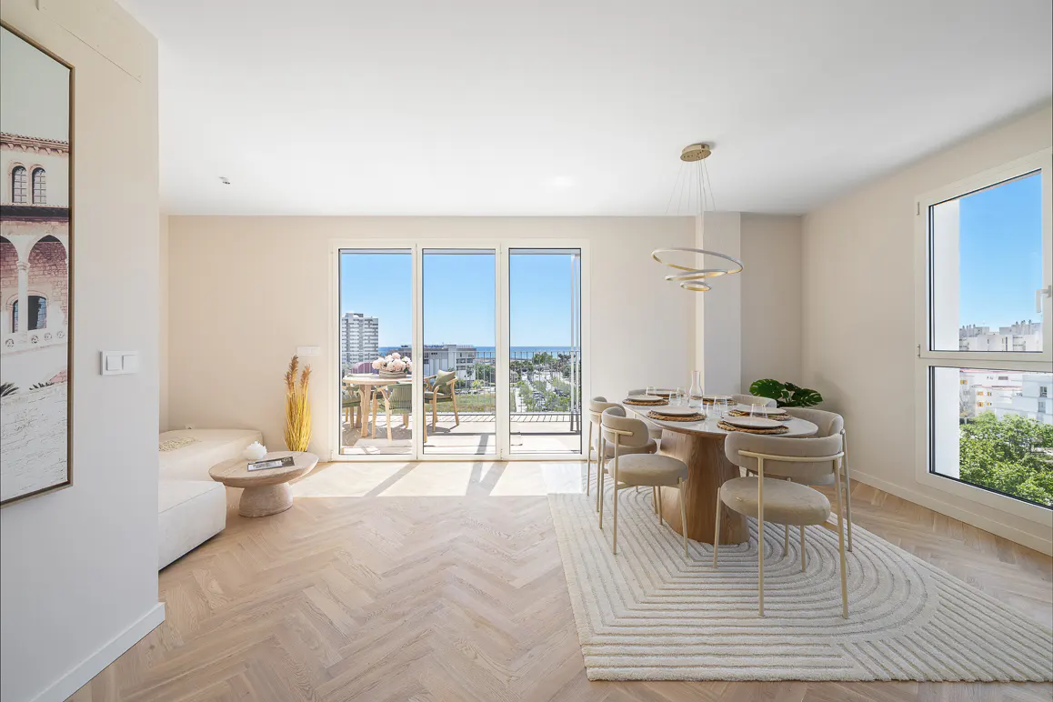 Bright, modern dining room with a round table, six chairs, and a balcony with ocean views. Neutral color palette with herringbone wood floors.