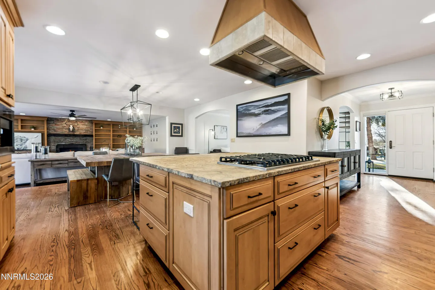 A bright, open kitchen with a large island, wood floors, and a view into the living room.