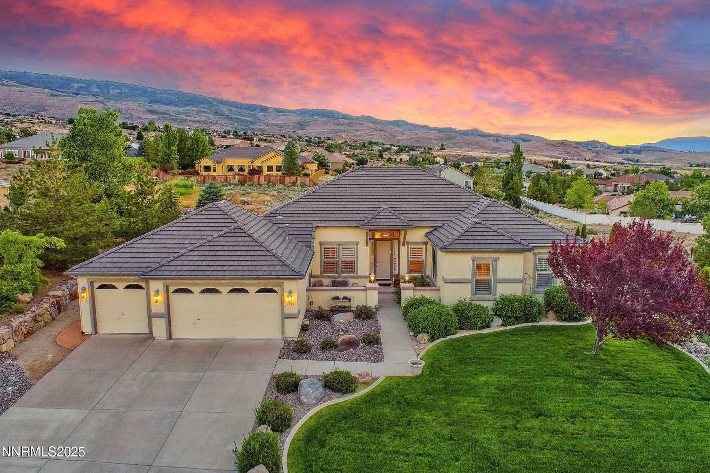 Aerial view of a tan house with a brown roof, green lawn, and a colorful sunset sky.