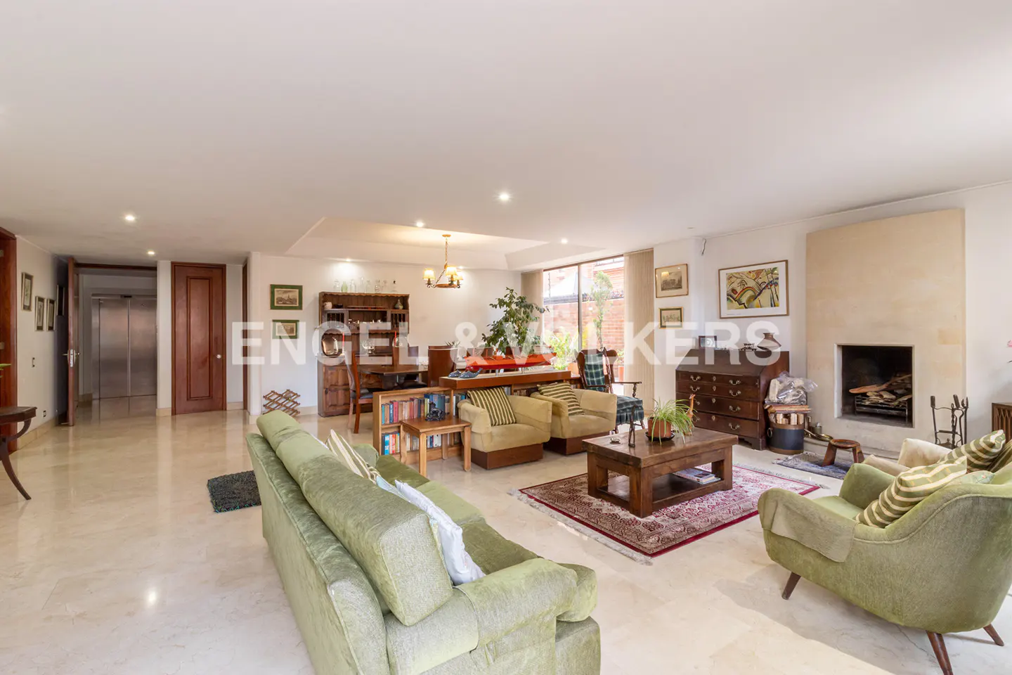 A spacious living room with green sofas, armchairs, a fireplace, and a dining area.