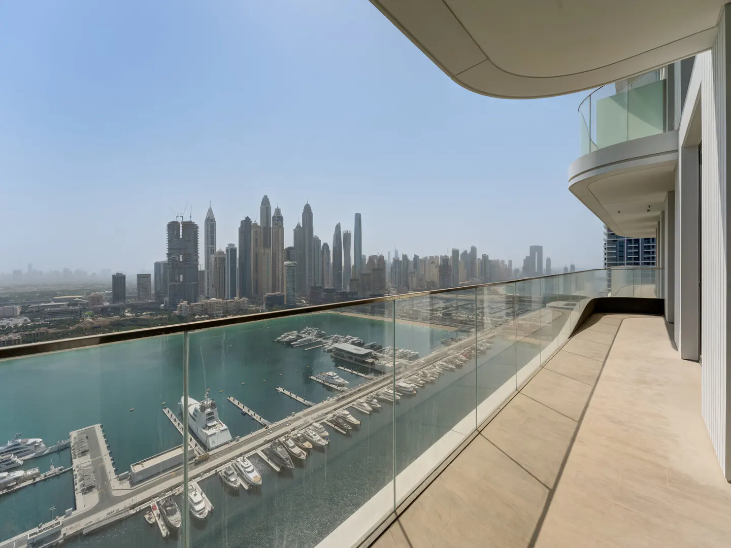 View from a high-rise balcony overlooking a marina filled with yachts and a city skyline under a hazy sky.