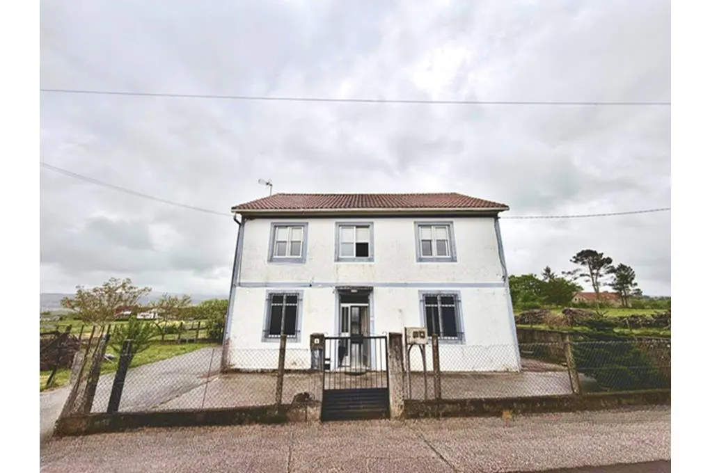 Two-story white house with a red tile roof, blue window trim, and a black metal fence on a cloudy day.