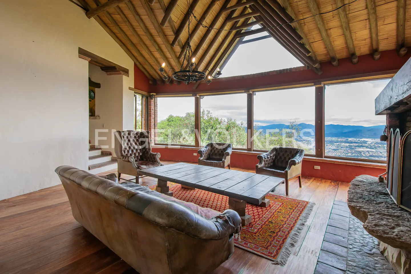 Rustic living room with vaulted wood ceiling, leather furniture, and large windows overlooking a scenic mountain valley.