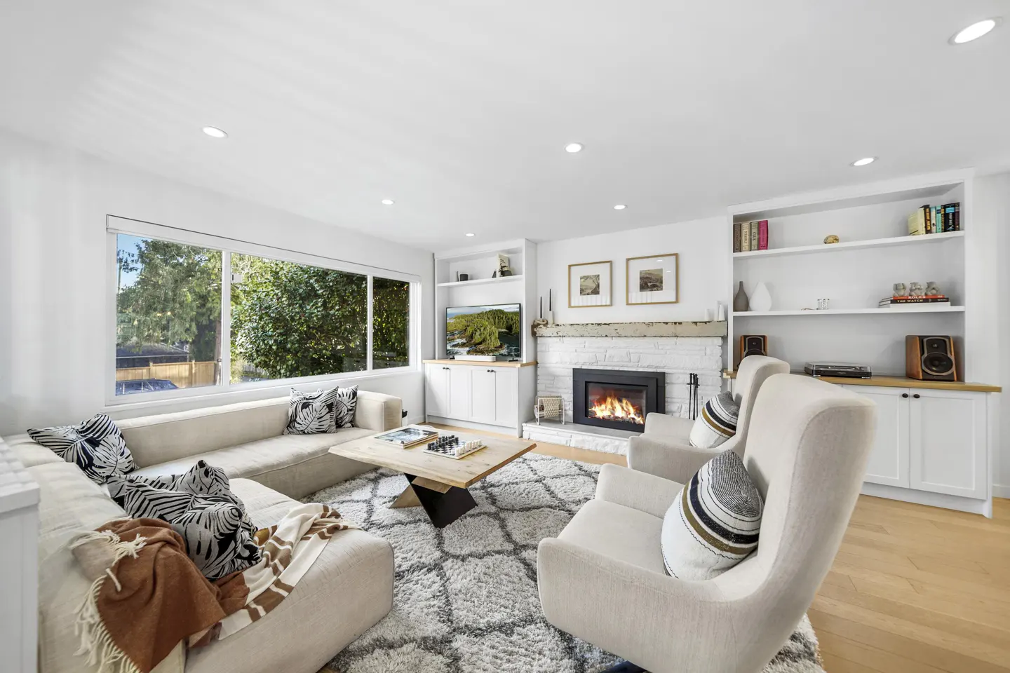 Bright living room with a white brick fireplace, a beige sectional sofa, and two armchairs on a patterned rug.