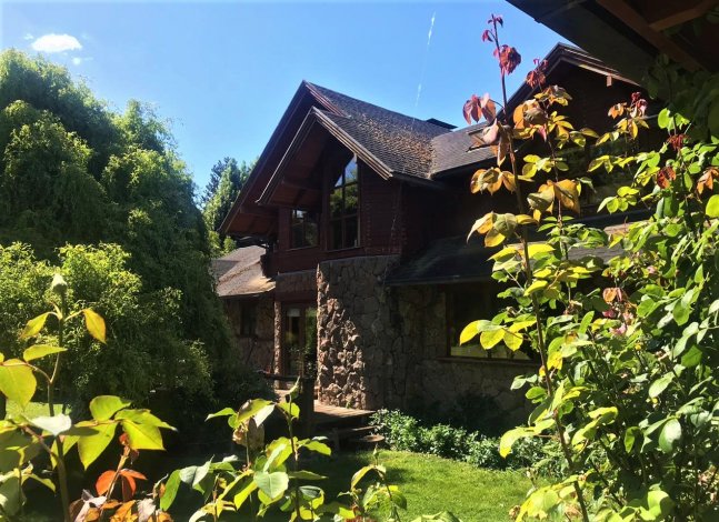 A two-story house with stone and wood siding, a dark roof, and green foliage.