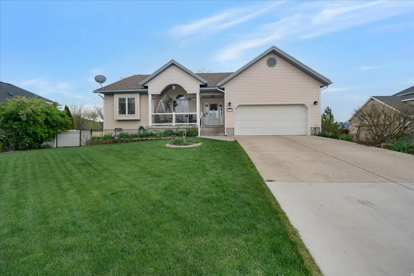 Beige single-story house with a white garage door, porch swing, and green lawn under a blue sky.
