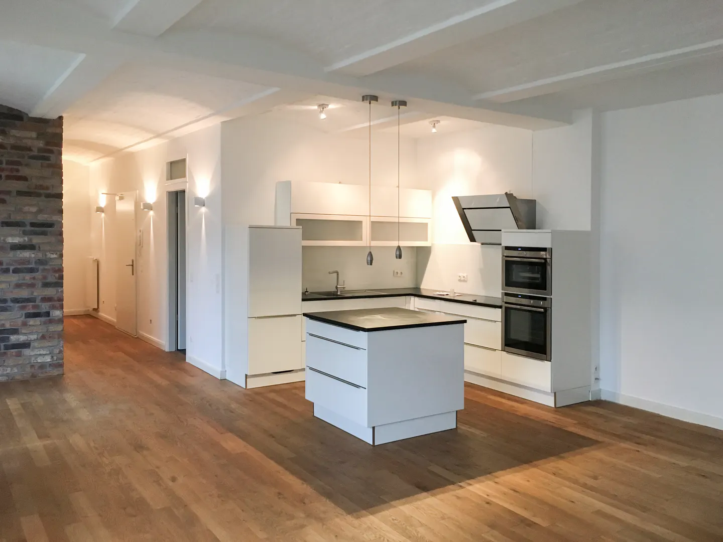 Bright, open-concept kitchen with white cabinets, island, and stainless steel appliances. Hardwood floors and exposed brick add warmth.