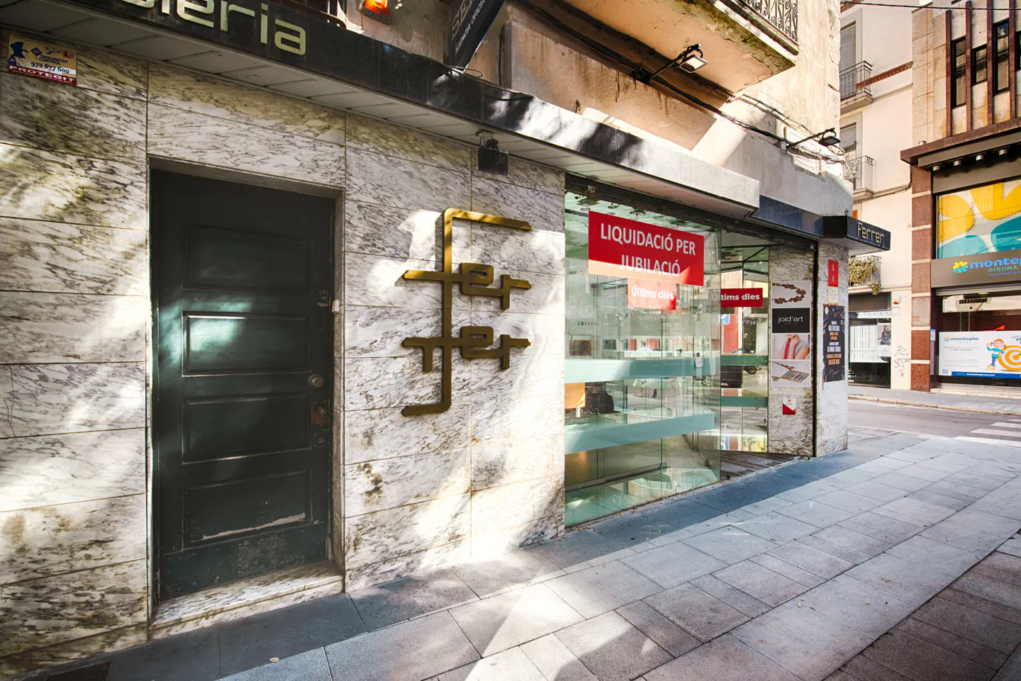 Storefront with marble facade, dark door, and a red "Liquidation for retirement" sign in the glass display window.