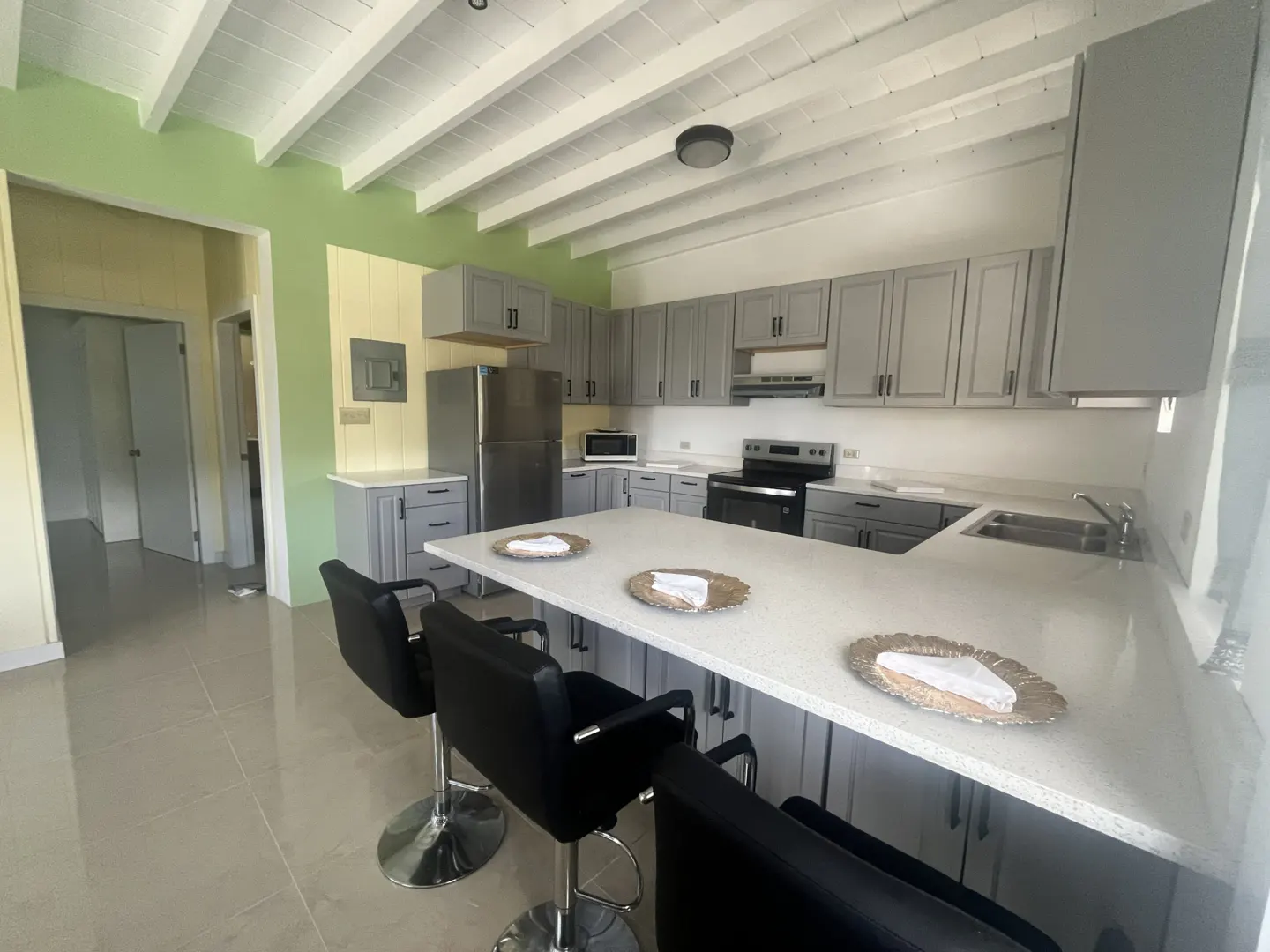 A bright kitchen with gray cabinets, stainless steel appliances, and a white countertop island with three black bar stools.