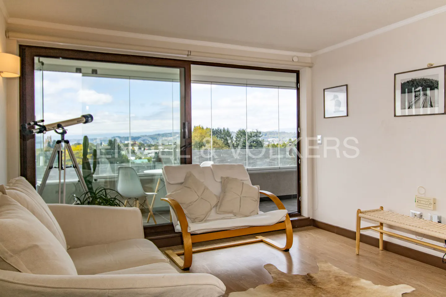 Living room with a telescope on a tripod by a sliding glass door to a balcony with a view. A white sofa and loveseat face the balcony.