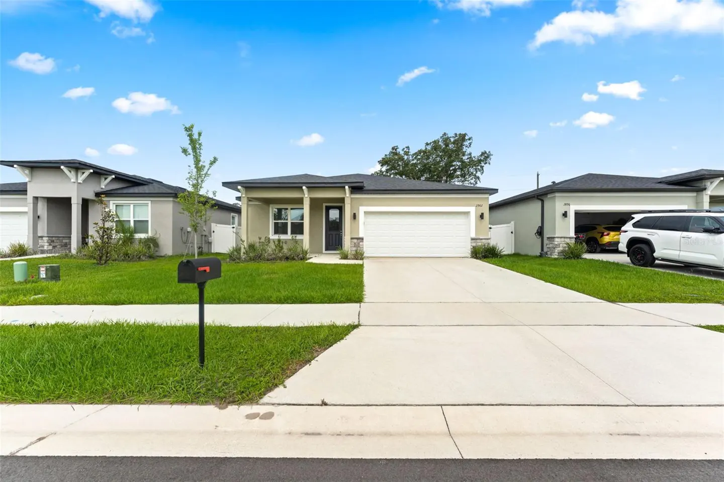 Single-story suburban home with a white garage, concrete driveway, green lawn, and a mailbox under a bright blue sky.
