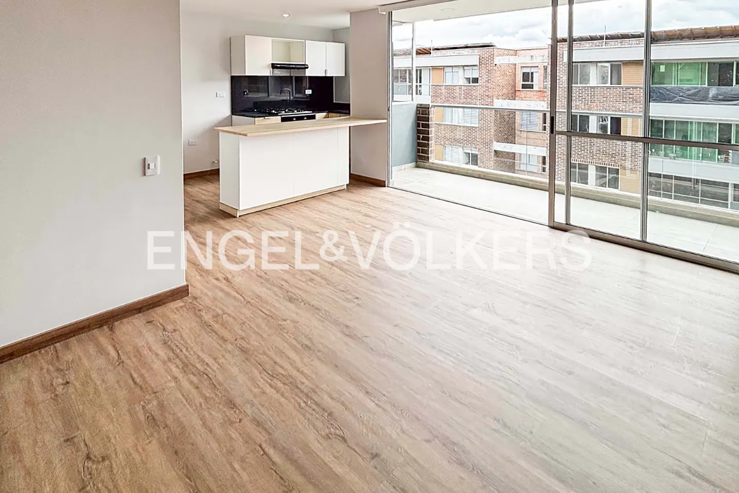 Open-concept apartment with wood floors, white kitchen cabinets, and a breakfast bar. Sliding glass doors lead to a balcony with city views.
