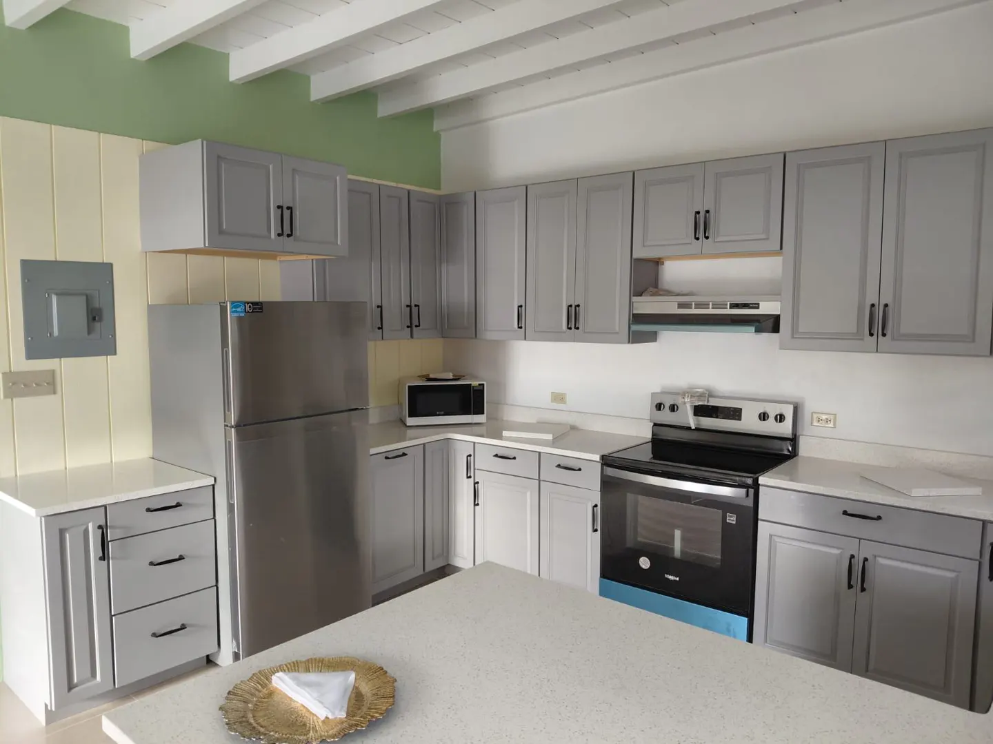 Bright kitchen with gray cabinets, black hardware, stainless steel appliances, and white countertops.