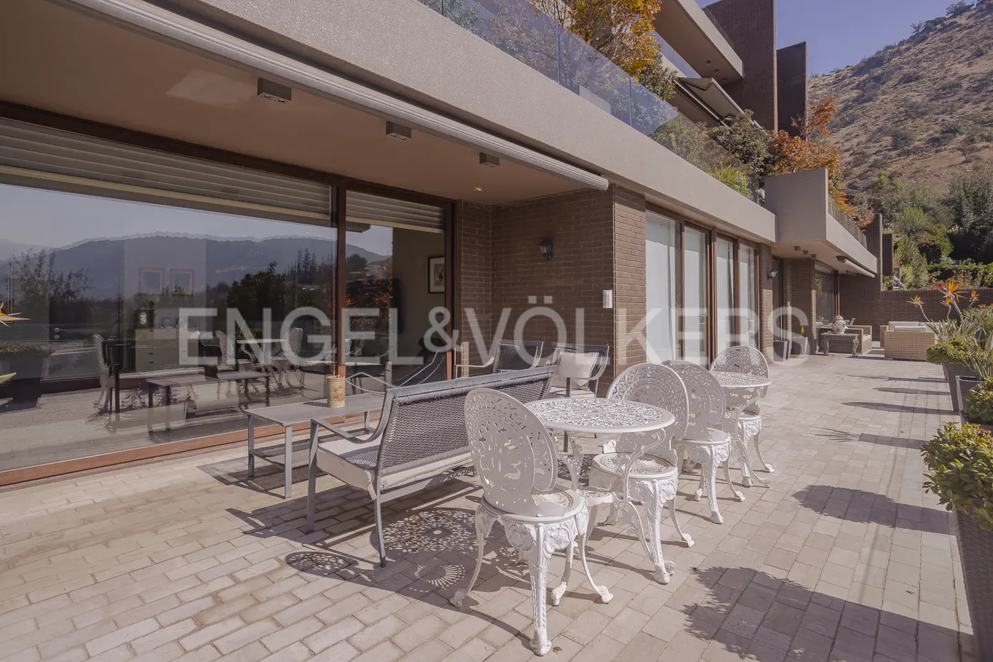 Spacious outdoor patio with white ornate metal furniture, a grey sofa, and brick walls, set against a mountain backdrop.