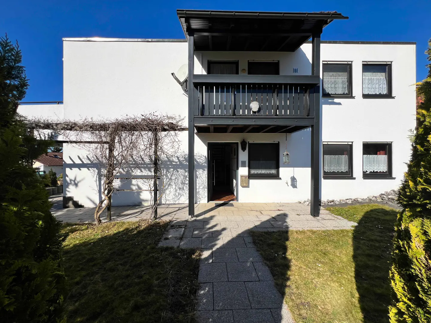 Two-story white house with a black balcony and trim, a stone walkway, and a green lawn under a clear blue sky.