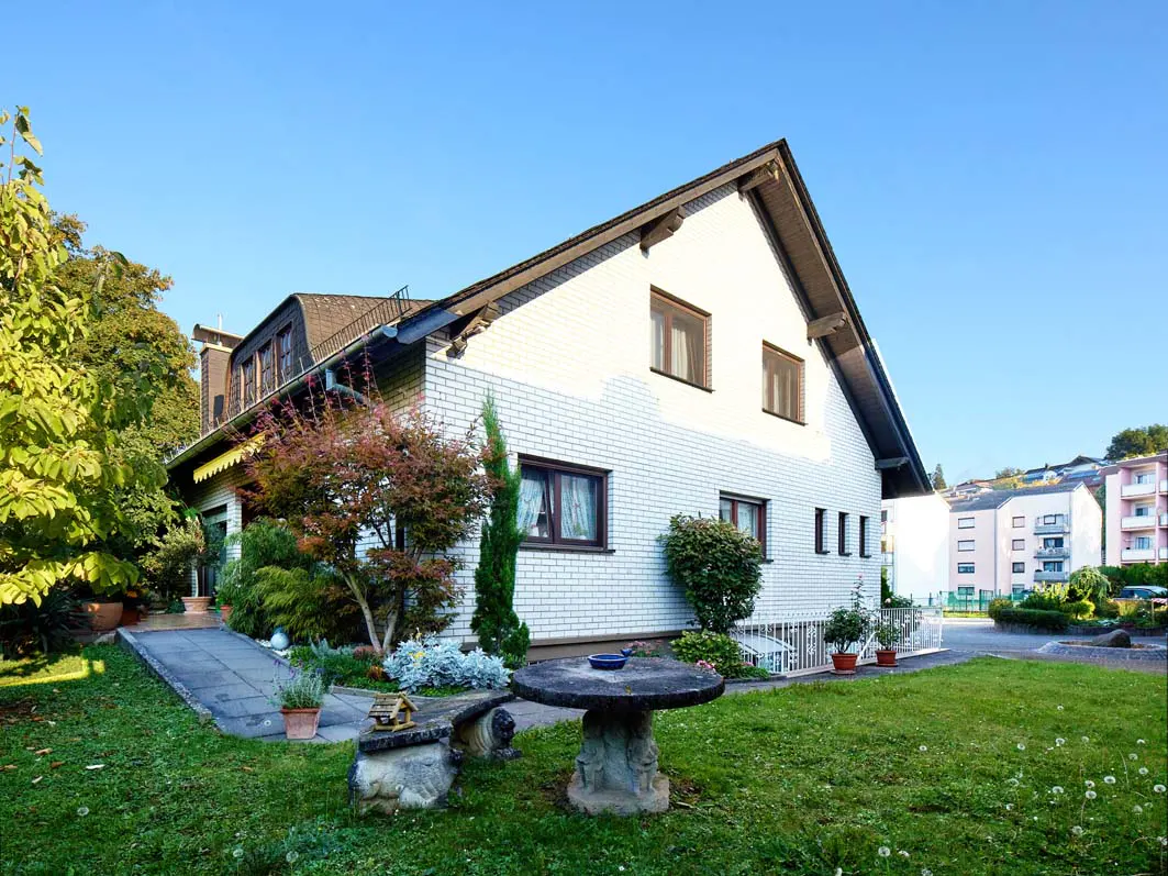Two-story white brick house with brown trim and a green lawn. A stone table and bench sit in the yard.