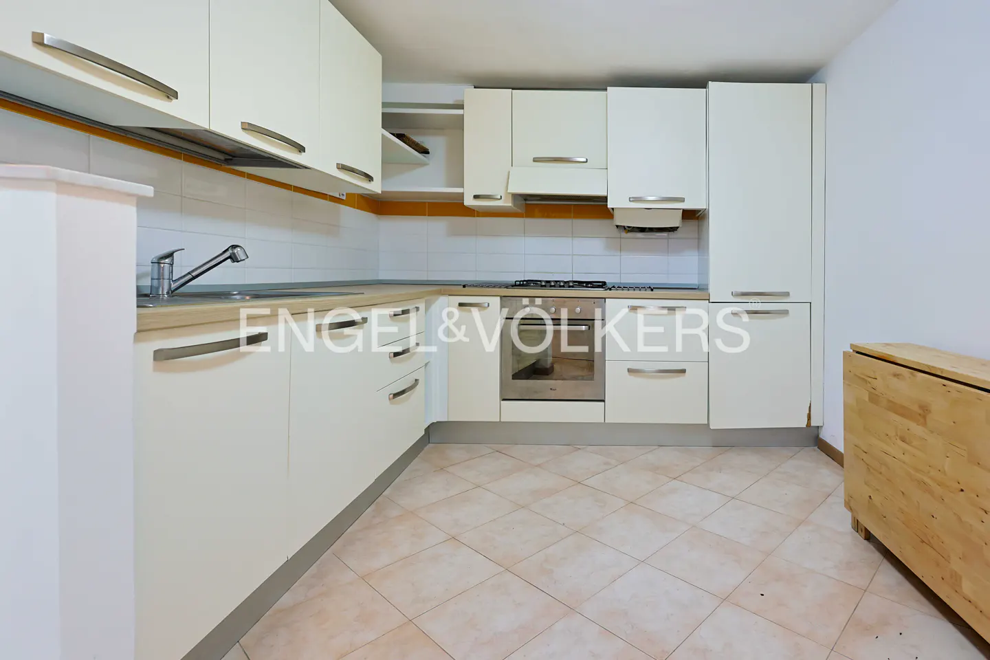 Bright kitchen with white cabinets, stainless steel handles, beige countertops, and a gas stove. Tiled floor and backsplash.