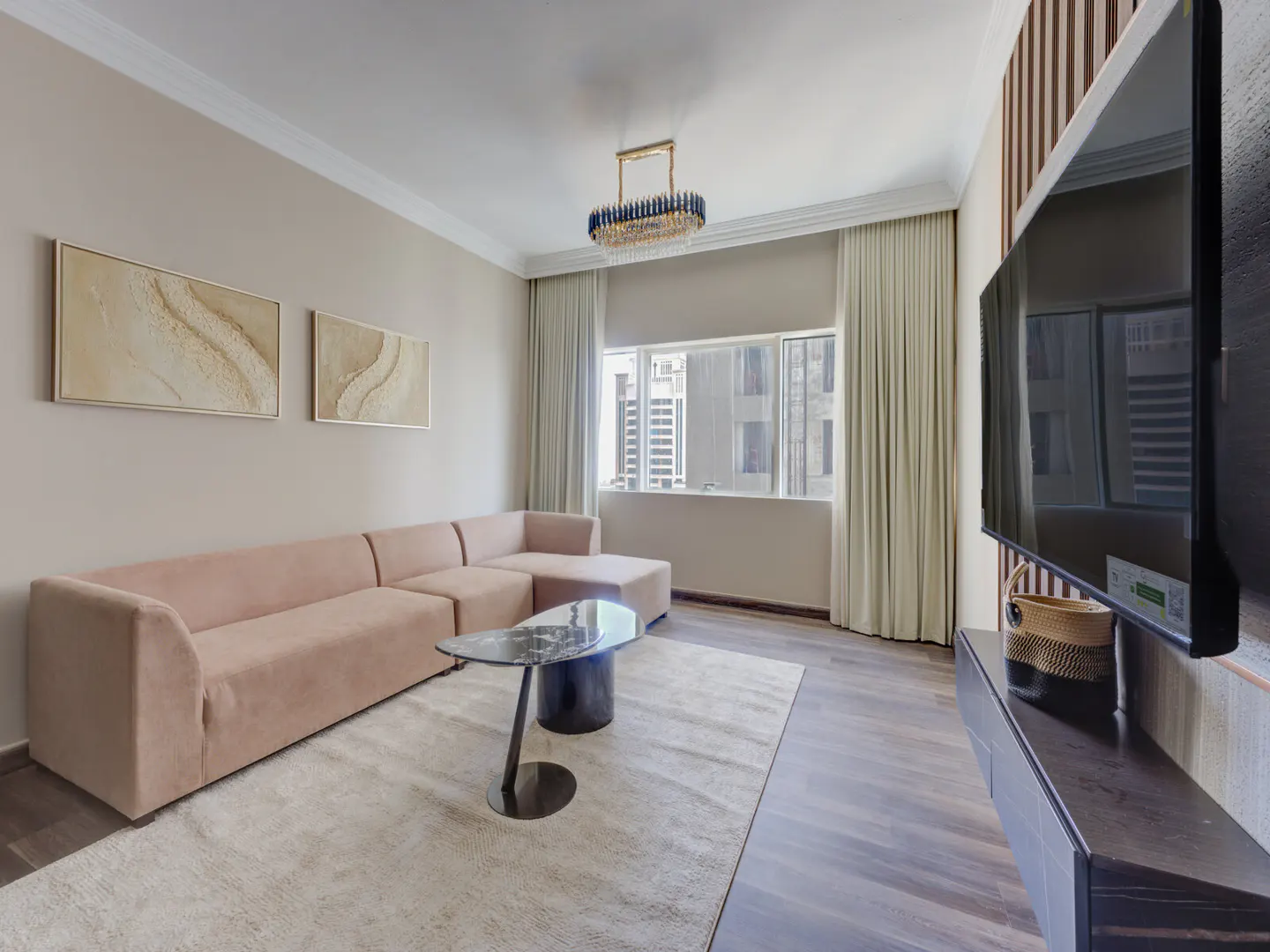 Living room with a pink sectional sofa, marble coffee table, and a large TV mounted on a wood-paneled wall. Two abstract paintings hang above the sofa.