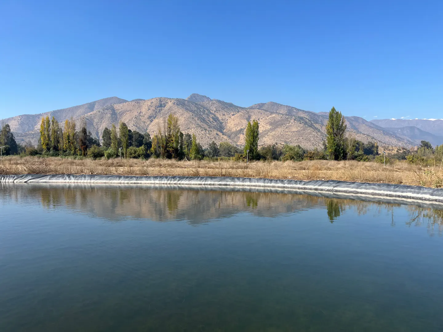 A wide shot of a pond with mountains in the background under a clear blue sky.