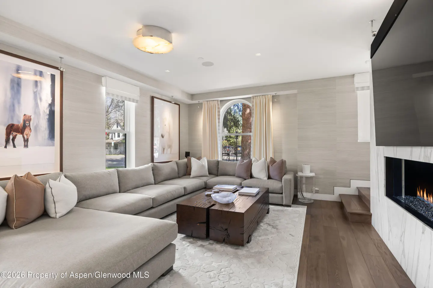 Living room with a gray sectional sofa, a dark wood coffee table, and a fireplace with a TV above it. Two large framed pictures hang on the wall.