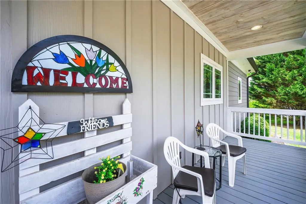 Front porch view with white chairs, a small table, and a "Welcome" sign with colorful flowers. A "Welcome Friends" sign is also visible.
