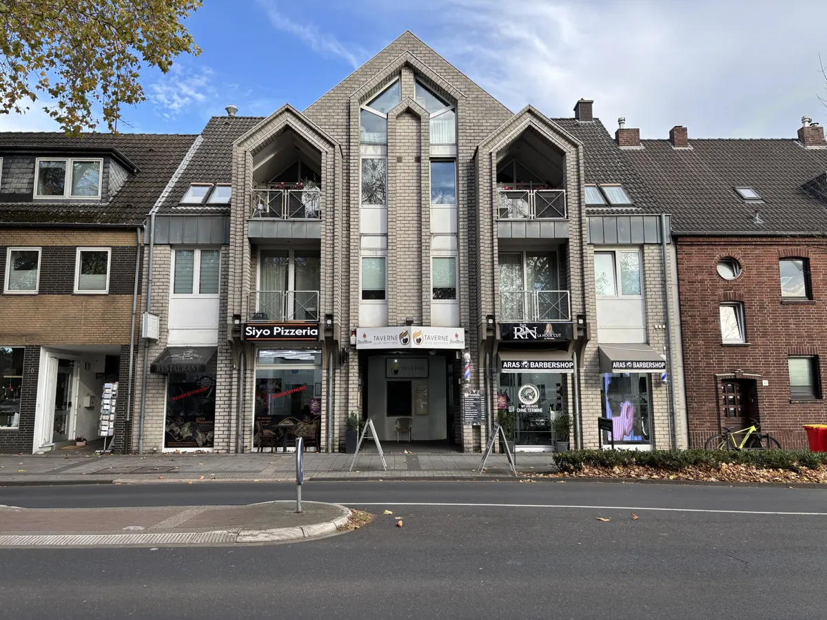 A street view of a row of buildings with businesses, including a pizzeria and barbershop, under a blue sky.