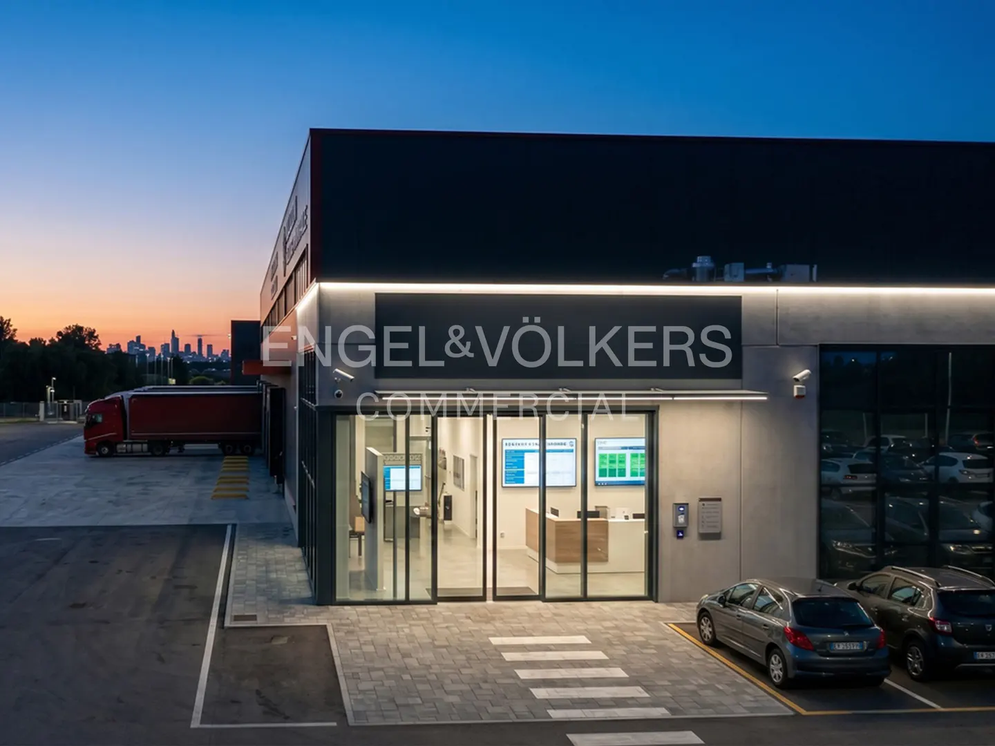 Exterior view of Engel & Völkers Commercial building at dusk, with parked cars and a truck visible.