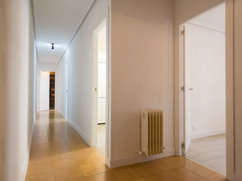 Hallway with light-yellow tile floor, white walls, and white doors. A radiator is on the wall.