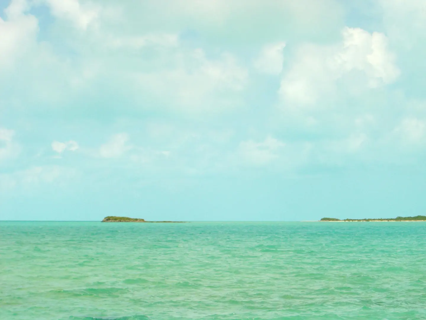 Turquoise ocean view with two small islands on the horizon under a cloudy sky.