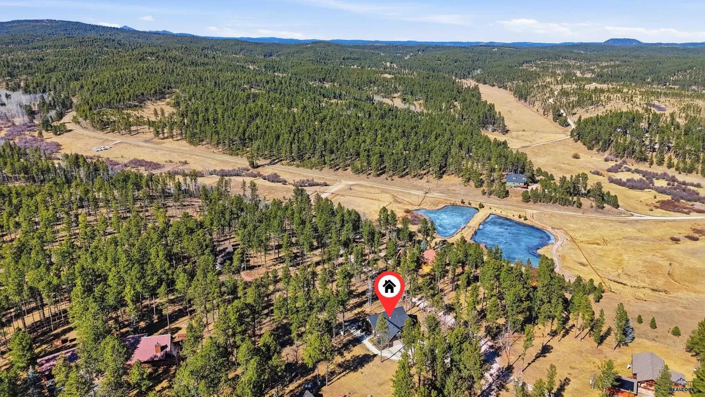 Aerial view of a home nestled in a dense pine forest with two small ponds nearby, marked by a red house location pin.