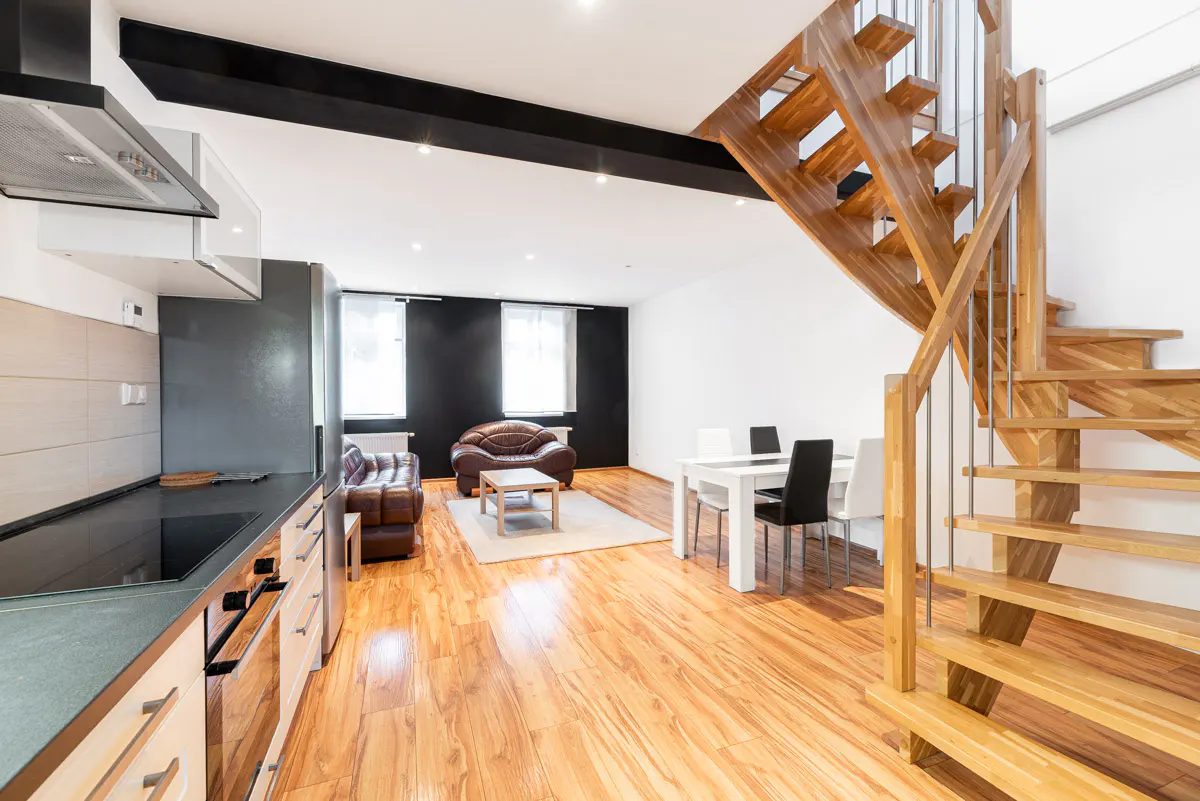 Open-concept living space with wood floors, kitchen, brown leather sofas, white table with black and white chairs, and wooden spiral staircase.