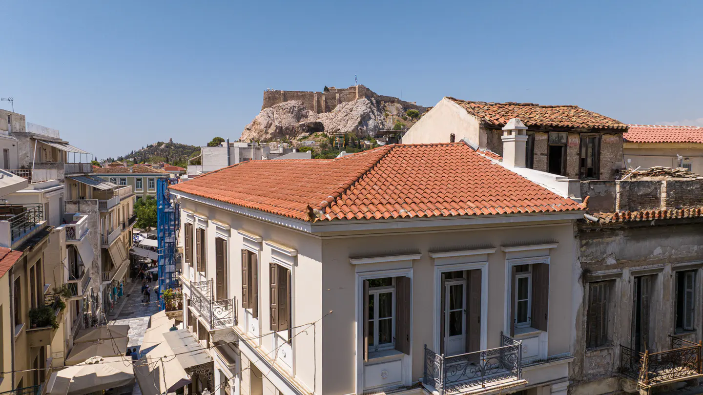 View of Athens buildings with red tile roofs and the Acropolis in the background on a clear, sunny day.